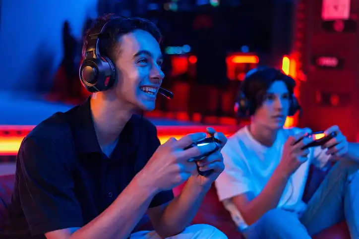Twee jonge mannen die glimlachen en geconcentreerd zijn terwijl ze videogames spelen met controllers in een levendige speelhal, waardoor een levendige en leuke sfeer ontstaat.